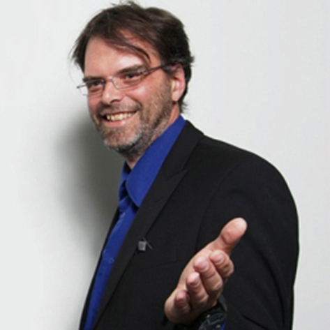 Colin gesturing with his hand toward the camera, smiling.